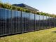 Solarzaun aus dunklen bifazialen Photovoltaikmodulen als Grundstücksgrenze mit Rasen davor